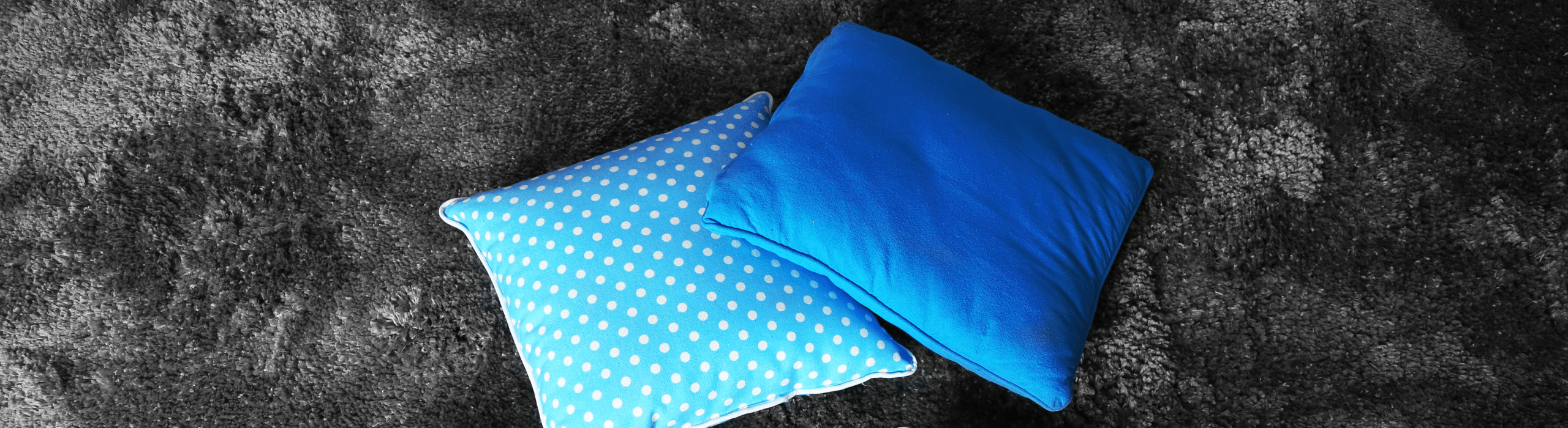Two blue pillows on top of dark gray carpet