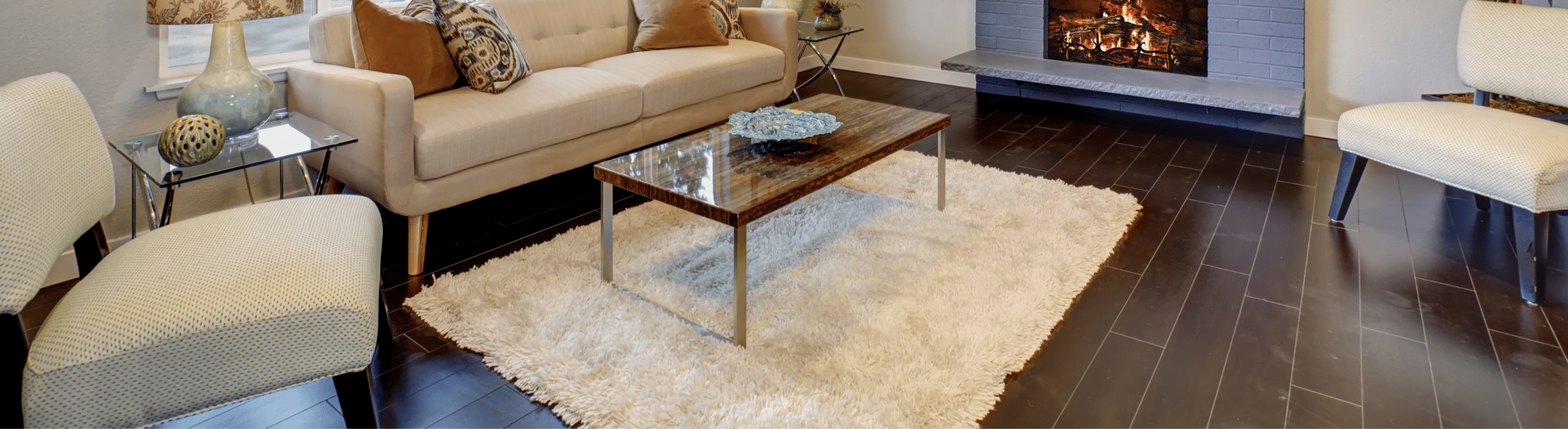 Living room with couch, chair, fireplace, and light colored rug on dark wood floor