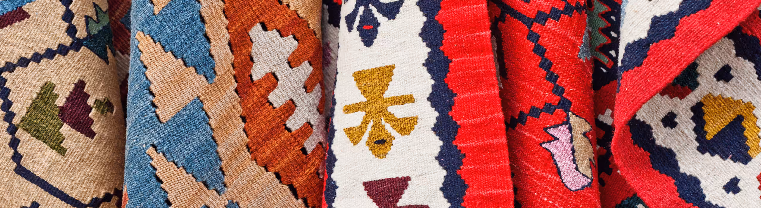 Detail of hanging collection of kilim rugs, featuring several colors and designs