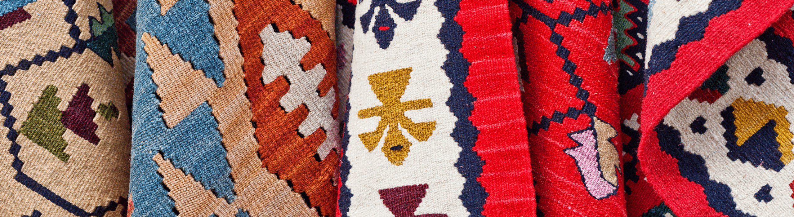 Detail of hanging collection of kilim rugs, featuring several colors and designs