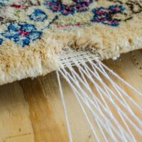 Rug with tear being professionally repaired using knotting method