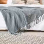 Bed with white comforter and green blanket with several area rugs on floor