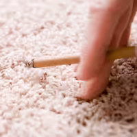 Fingers holding cigarette next to rug causing odors
