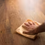 Male hand cleaning and rubbing an hardwood floor with a microfiber cloth.
